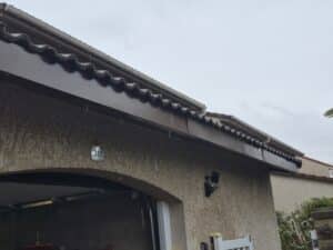 Pluie s'écoulant du toit d'une maison au mur crépi avec le numéro 351 visible au-dessus d'un garage.